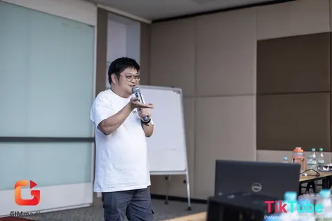 Mike memegang mikrofon sambil berbicara dengan peserta di dalam bilik bengkel.